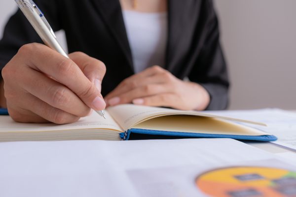 The woman is writing a message in the book on table. He is now sitting business plan that has new idea in the morning. Concept idea planing and analyzes.