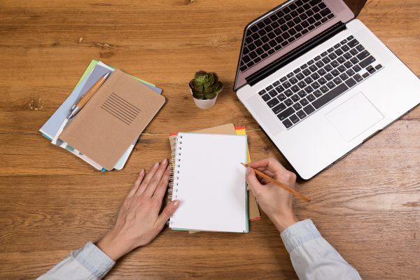 Woman working with laptop on old wood table. Mix of office supplies and gadgets on a wooden desk background. copy space.