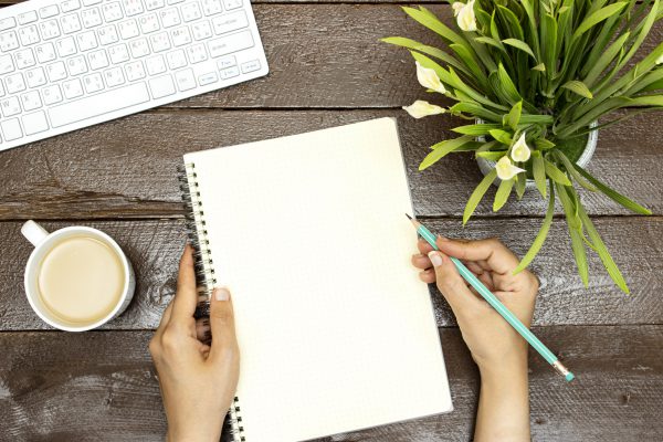 workspace : modern laptop with copy space, lilies flowers  and milk coffee cup and hands writing on empty notebook on wooden table