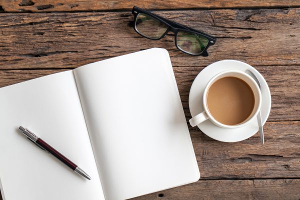 Blank paper with pen and cup of coffee on wooden table